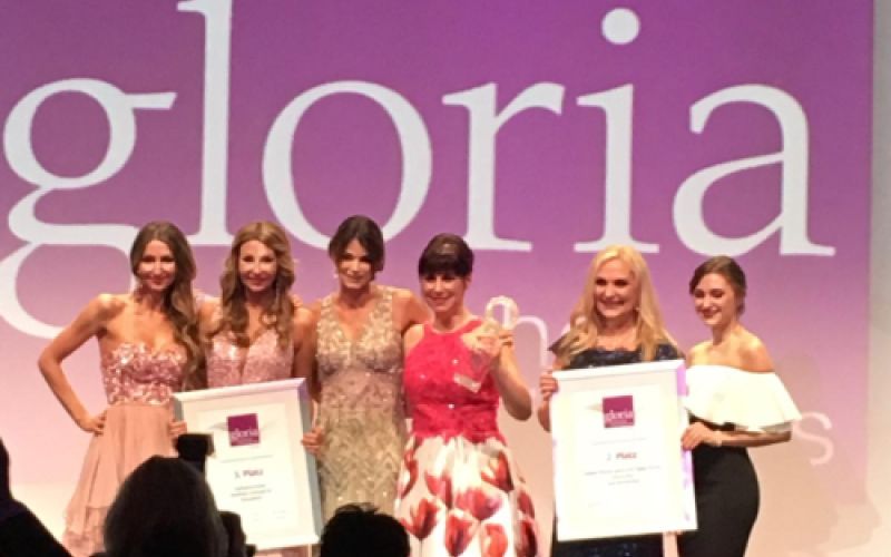 Claudia Singer im roten Kleid mit Award zwischen Preistraegerinnen vor Gloria-Wand